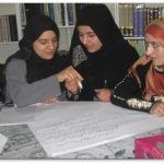 Three Afghan girls writing on a sheet of paper