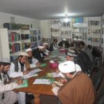 Afghan imams gathered at a table, writing on pieces of paper
